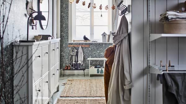 Deux range-chaussures HEMNES blancs à 4 compartiments sont installés dans une entrée lumineuse en face de vêtements suspendus à des crochets.