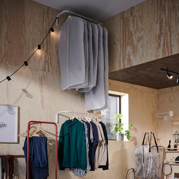 Deux tringles à vêtements sont fixées au mur. L’une, contre le plafond, accueille les vêtements sous housse, et l’autre, plus bas, est à portée de main.