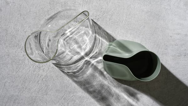 Deux vases-arrosoirs CHILIFRUKT en verre clair et en acier vert placés sur une surface en ciment gris.