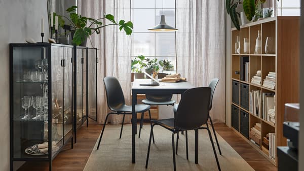 Deux vitrines noires RUDSTA le long du mur, avec une table de salle à manger SANDSBERG noire et des chaises LIDÅS dans la lumière.