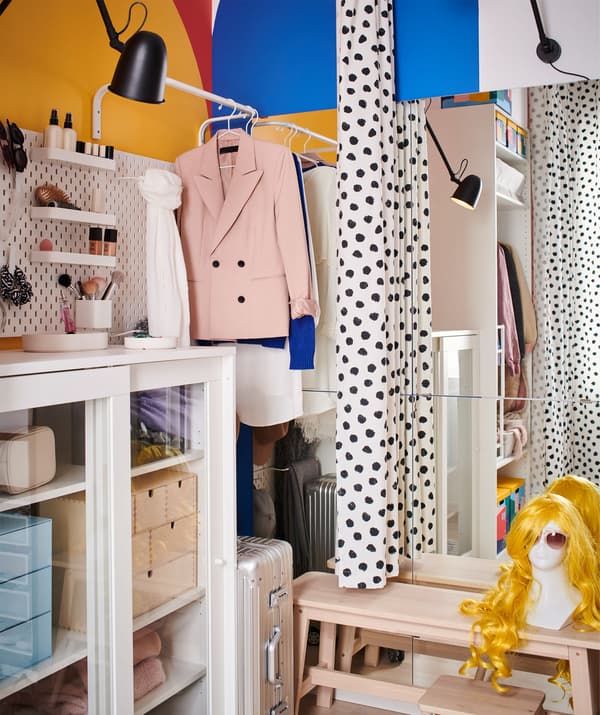 Deux zones d'une même pièce, avec rangements et vêtements d'un côté d'un rideau, et banquette, miroir et éclairage de l'autre côté.