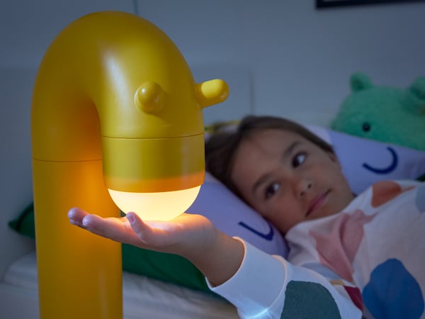 Děvčátko se dotýká žluté stojací lampy ve tvaru žirafy GREJSIMOJS.