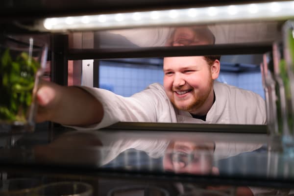 Devin Heusden lacht schuin richting de camera en pakt iets uit een kastje.