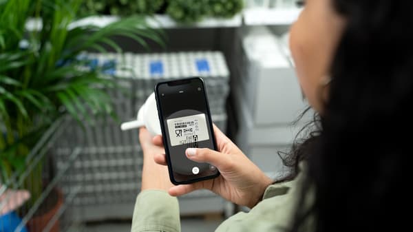 Devojka se nalazi u robnoj kući IKEA. U jednoj ruci drži telefon u drugoj telefon. Na telefonu je otvorena IKEA aplikacija i IKEA Scan opcija. Ona skenira proizvod.