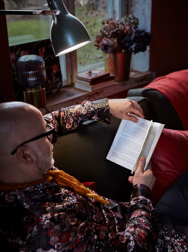Di ruang tamu yang selesa, seorang lelaki bersantai di atas sofa sambil membaca buku. Lampu lantai memberikan pencahayaan sambil dia membaca.