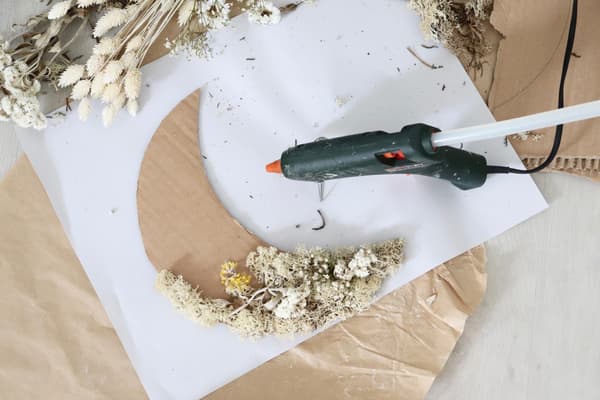 Die Blumen werden mit Heißkleber auf den Pappmond geklebt.