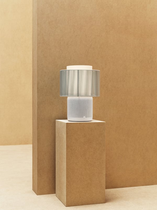 Die weiße IKEA SYMFONISK Tischleuchte steht vor einer braunen Wand.