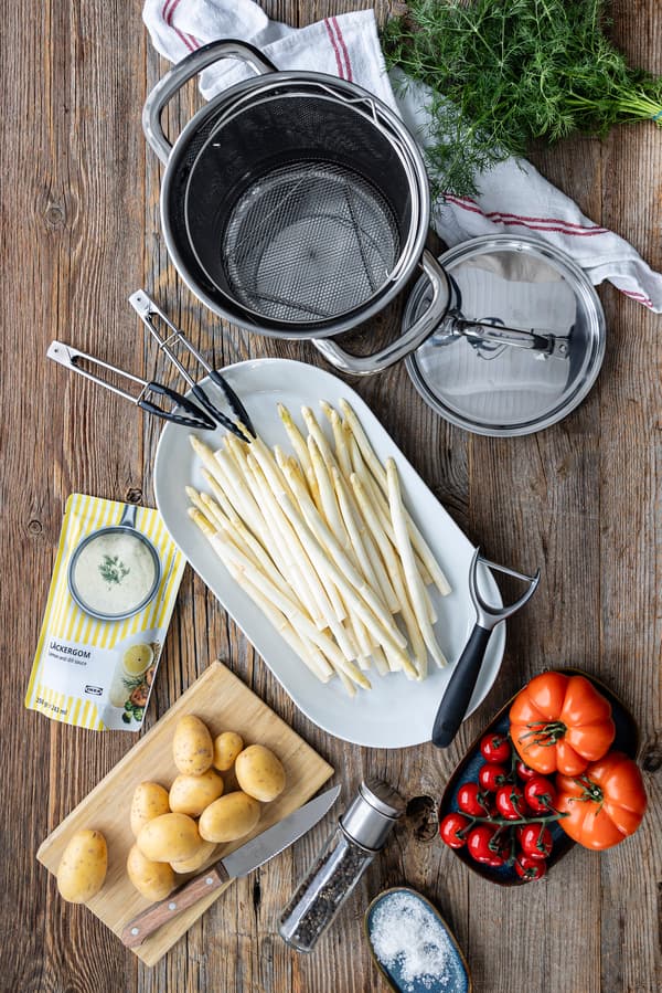 Die Zutaten für Spargel mit Kartoffeln, geschmorten Tomaten und Zitronen-Dill-Soße liegen auf einer Holzplatte.