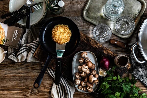 Die Zutaten für veganes Stroganoff neben einer Pfanne mit Kartoffelrösti.