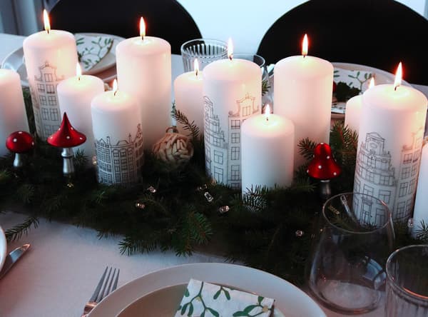 Dieci candele bianche accese con decorazioni natalizie su un tavolo da pranzo