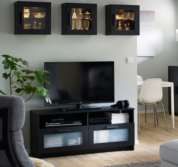 Diese schwarze, stilvolle BRIMNES TV-Bank verfügt über große Schubladenfronten aus Frostglas, mit der du Fernbedienungen und anderes TV-Zubehör ordnen kannst. Dank der Kabelöffnungen lassen sich Kabel kaum sichtbar hinter das Möbelstück führen, damit du sie trotzdem jederzeit erreichen kannst.