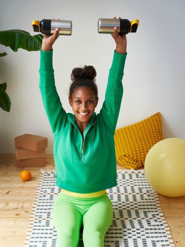 Dievča sedí na koberci VAMDRUP a posilňuje pomocou dvoch termosiek HETLEVRAD.