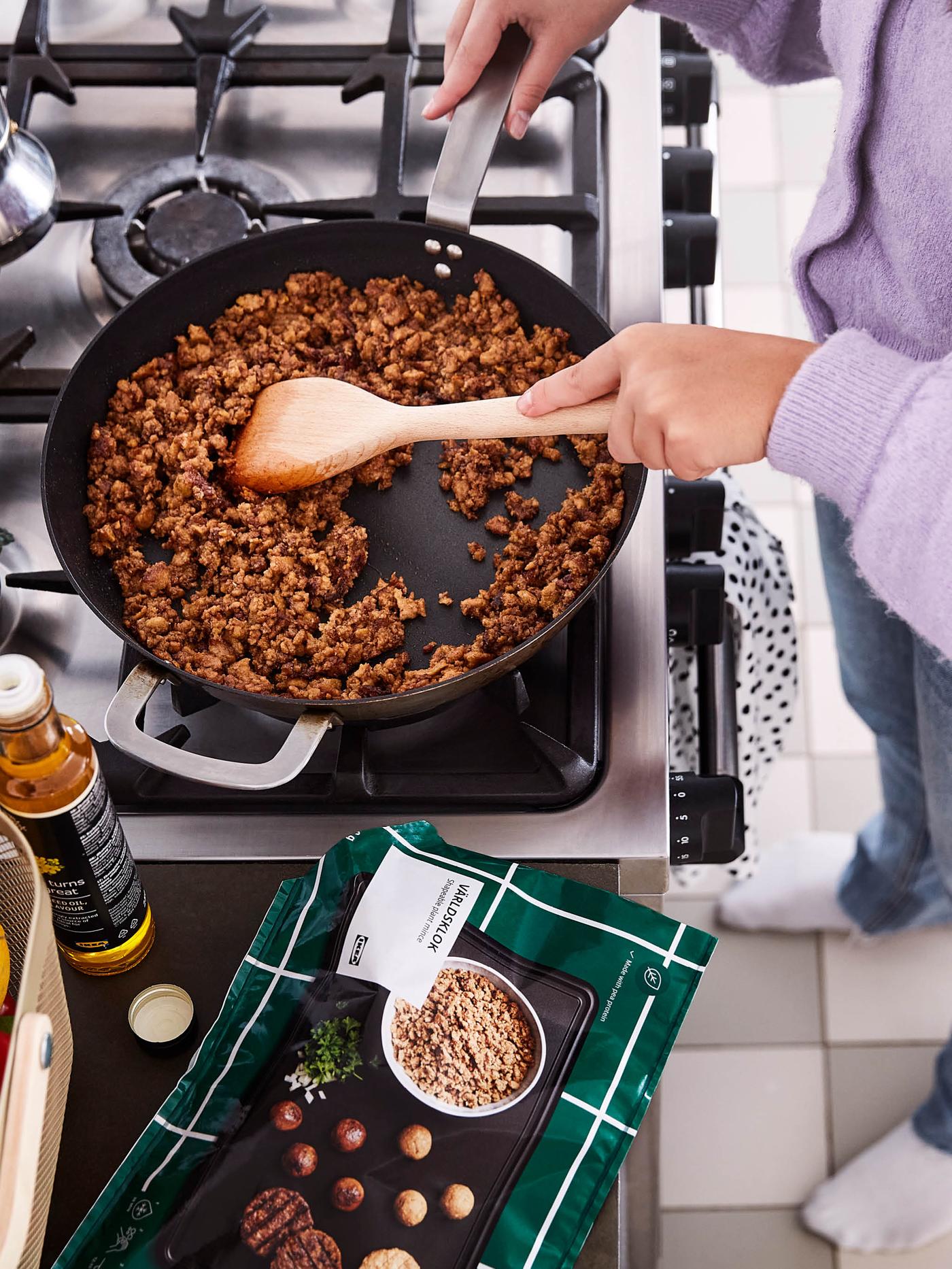 Dievča vo fialovom svetri mieša bezmäsitú zmes VÄRLDSKLOK v panvici VARDAGEN.