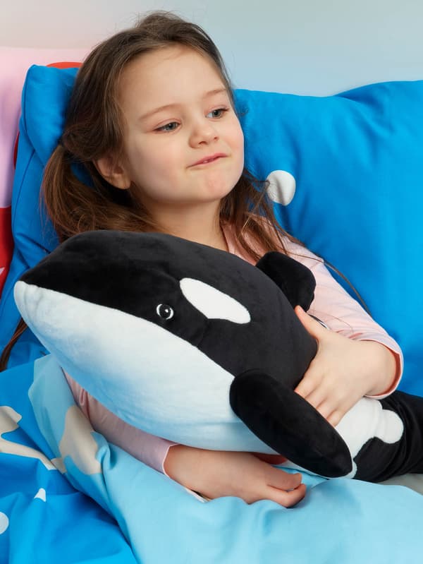 Dievčatko v posteli v modrej posteľnej bielizni BLÅVINGAD drží v náručí plyšovú kosatku BLÅVINGAD.  