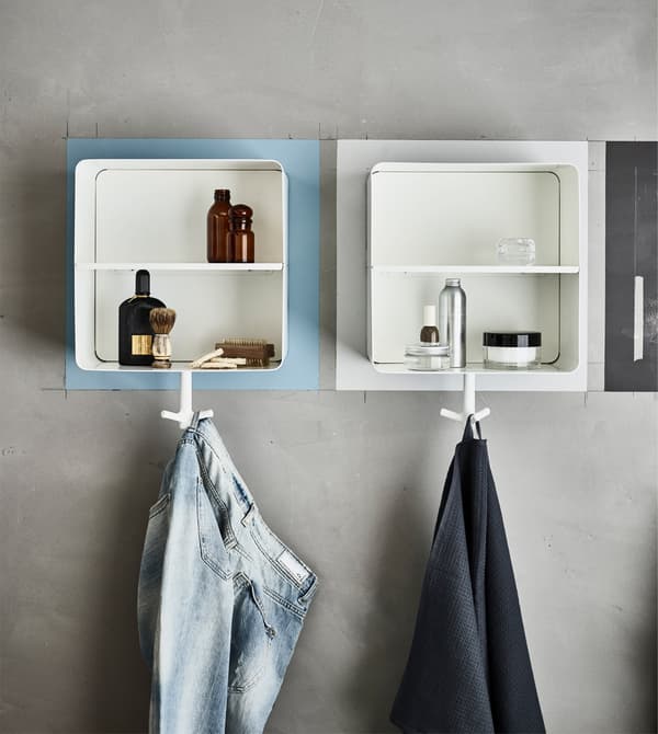 Different coloured wall cabinets in a bathroom containing bottles and shaving equipment and holding a towel and trousers.