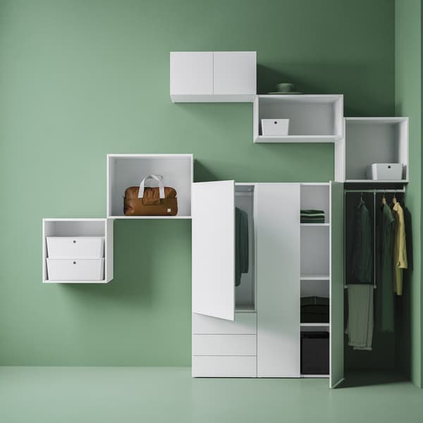 Different sizes of white PLATSA storage units placed on a green wall, with some doors open revealing folded and hung clothes.