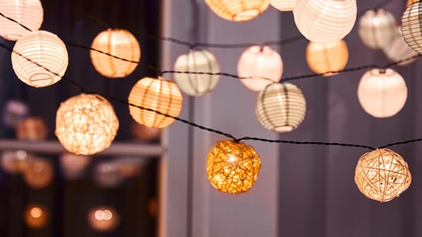 Different types of SOLVINDEN LED string lights hang on a balcony outside a window at night. The string lights are lit.