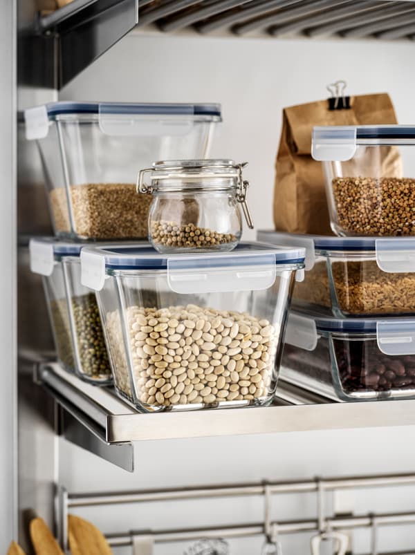 Différents aliments secs, des fèves, des lentilles et des céréales, dans des contenants pour aliments en verre IKEA 365+ rangés sur une tablette métallique de cuisine.