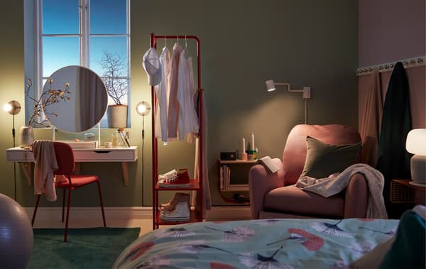 Dimly lit bedroom with a make-up nook, room-dividing clothes rack and reading corner with recliner.