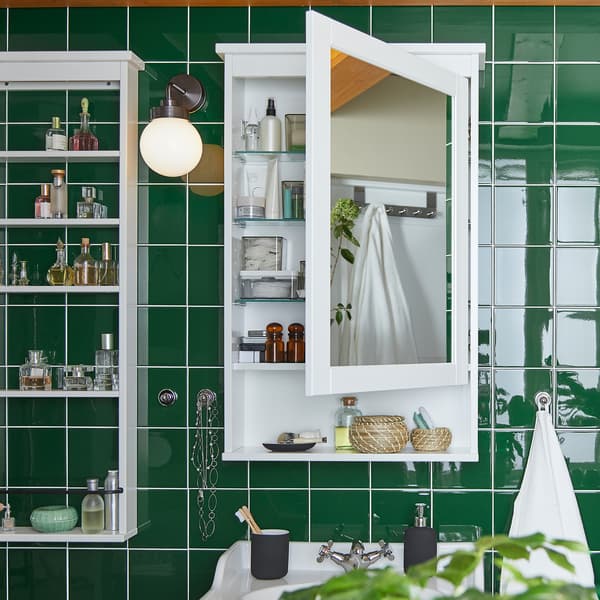 Dinding berjubin hijau dengan kabinet bercermin HEMNES berwarna putih yang dilekap di dinding. Kabinet bercermin ini terbuka dan semua produk berdiri di atas rak.