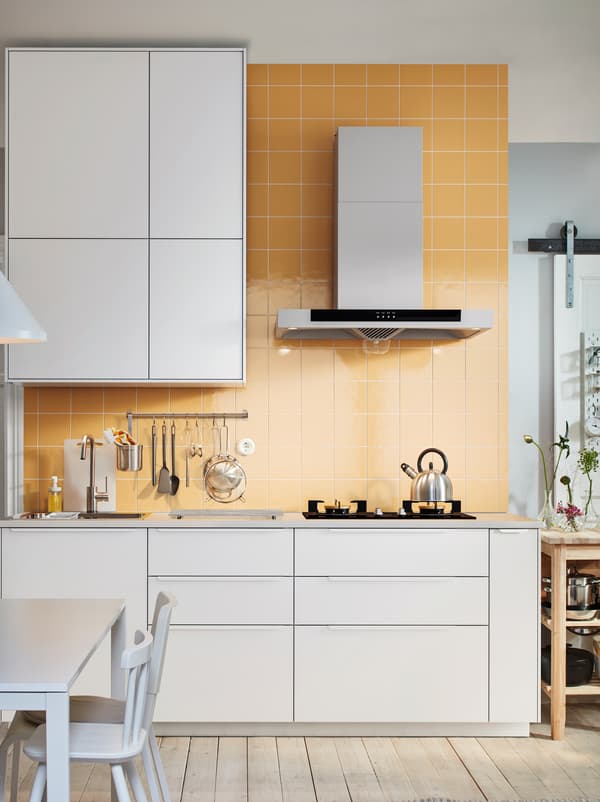 Dinding dapur berjubin berwarna coklat lembut. Permukaan atas kerja yang mempunyai sink, hob dan perkakas dapur, dibingkaikan di atas dan di bawah oleh barisan kabinet METOD berwarna putih.