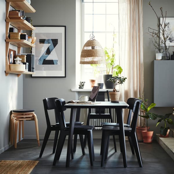 Dining area with a table, four chairs and a highchair in black, open shelves in ash veneer, four stools and beige curtains.