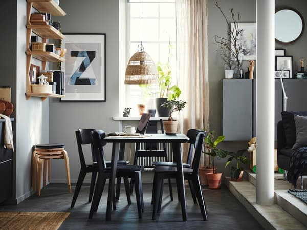 Dining area with a table, four chairs and a highchair in black, open shelves in ash veneer, four stools and beige curtains.