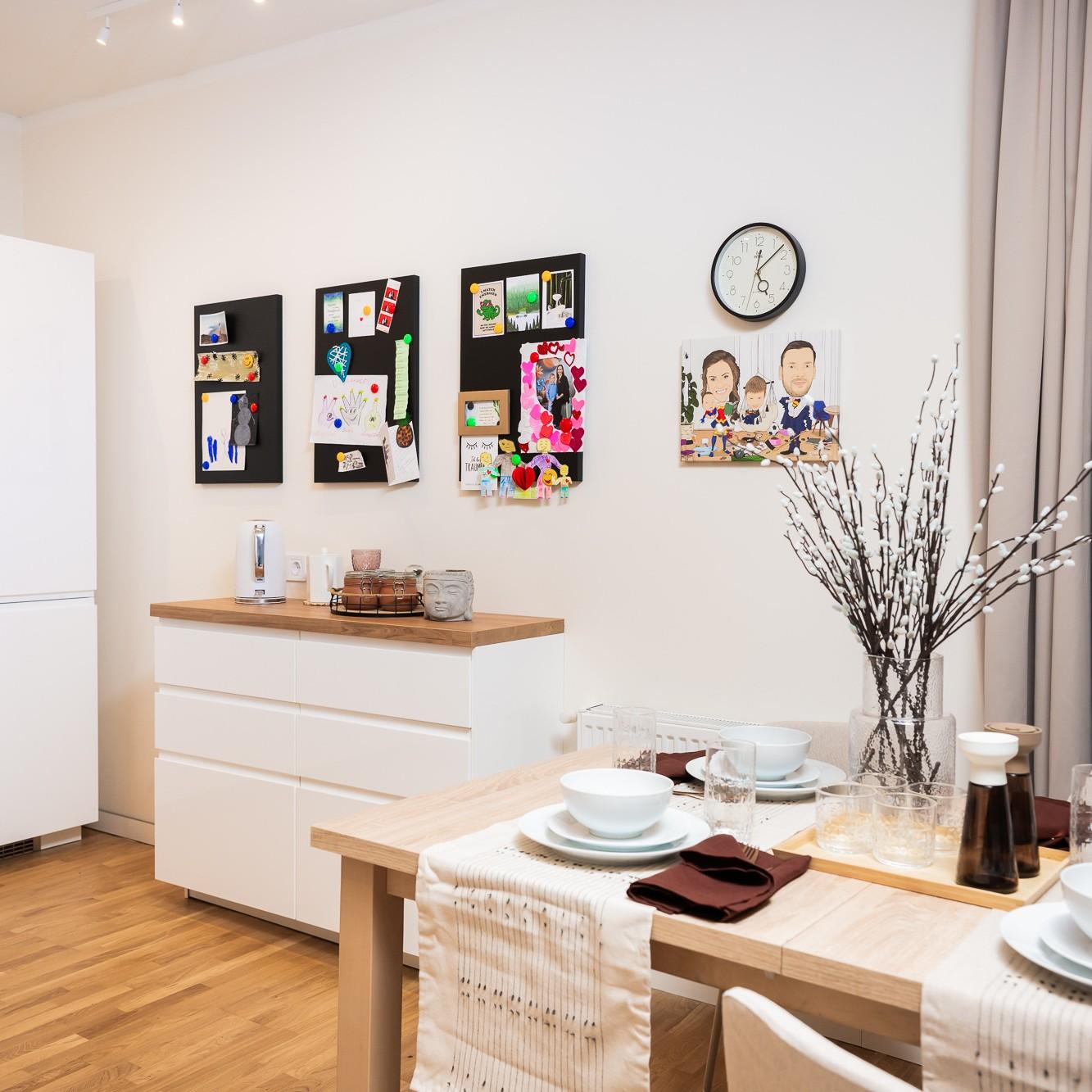 Dining area with a wooden table and white chairs, a white sideboard and wall décor in the background; a bright, organised and welcoming space.