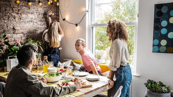 Dining room in which 4 people are about to sit down around a set table.