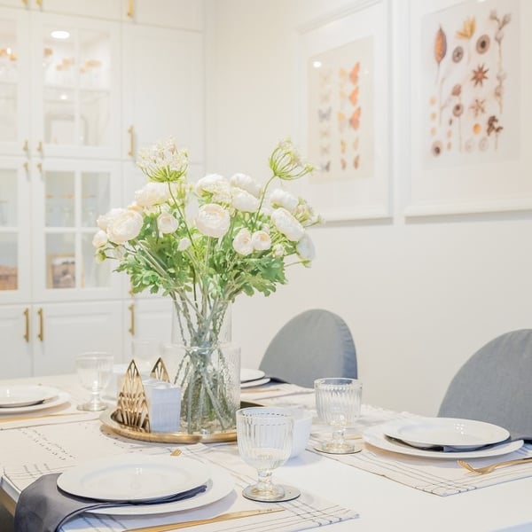 Dining table decorated with white flowers in glass vase and tableware set.