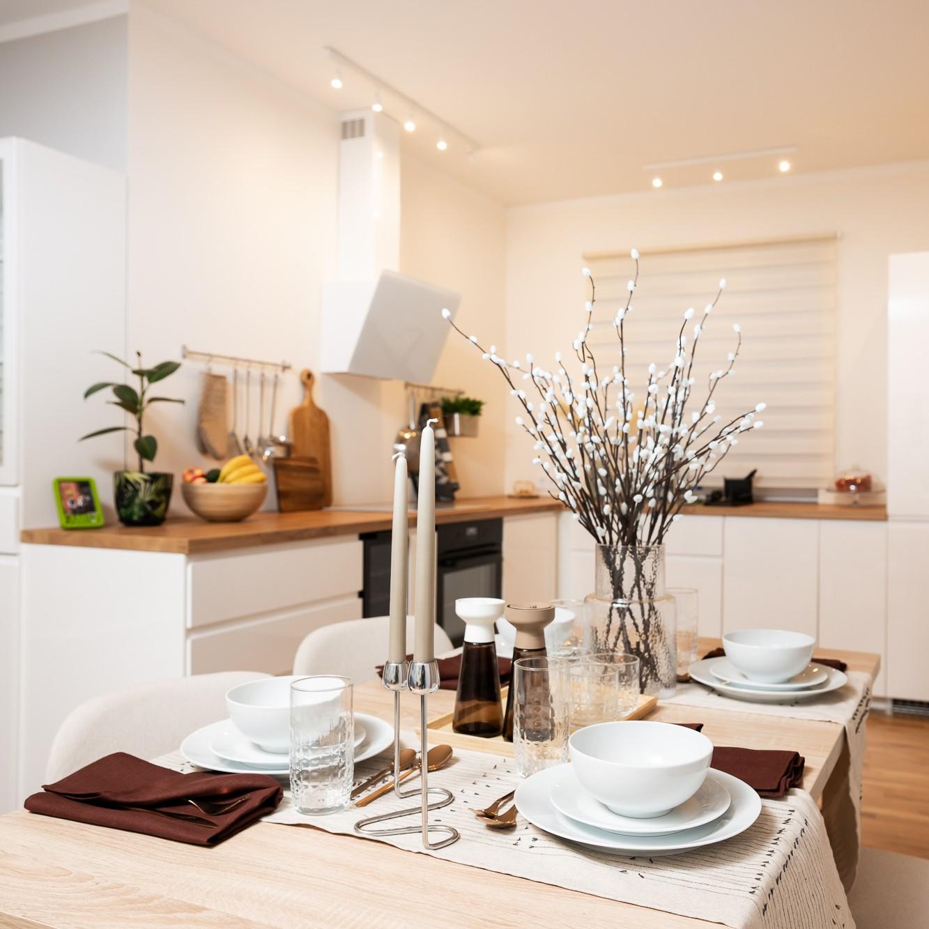 Dining table set with plates, glasses and napkins; the kitchen and wooden worktop visible in the background.