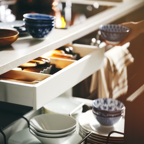 Dinnerware including patterned/blue ENTUSIASM bowls and side plates stacked in an open drawer below a kitchen worktop.