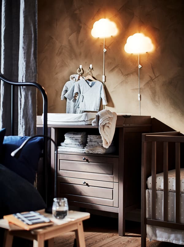 Dio spavaće sobe napola skriven iza zavjese koja dijeli prostoriju uz dječji krevetić i SUNDVIK stol za previjanje.