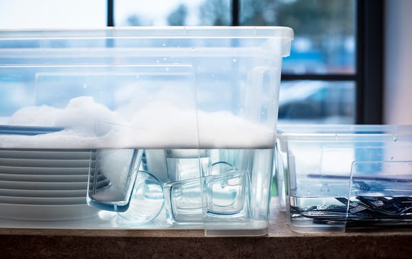 Dirty tableware soaking in clear plastic tubs of soapy water.