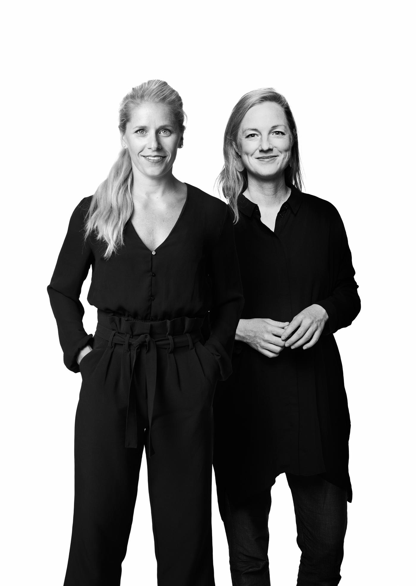 Diseñadoras en blanco y negro vestidas de negro y abrazadas.