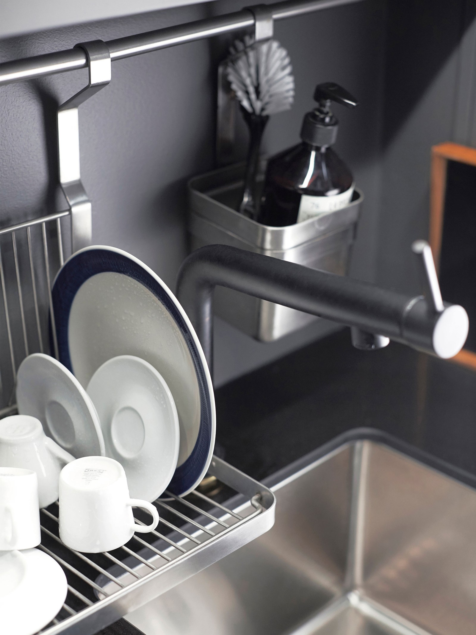 A hanging dish rack dries saucers, mugs and a plate next to the kitchen sink.