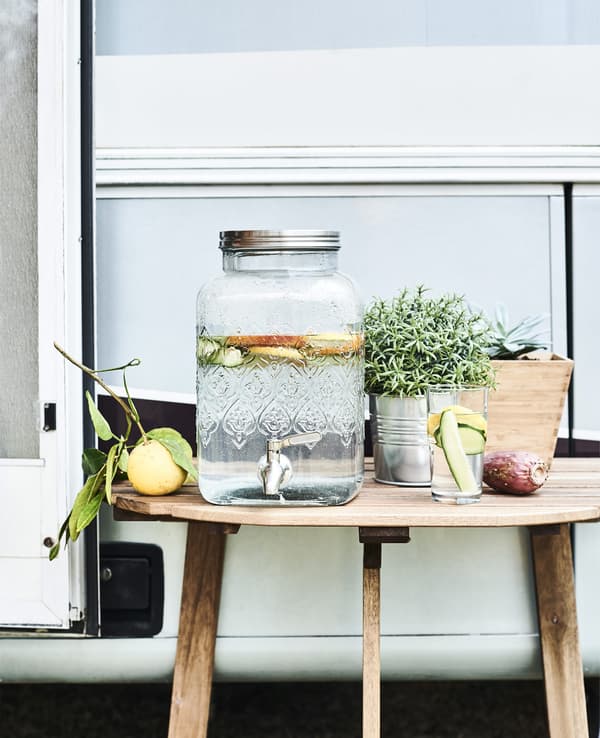 Dispenser in vetro con rubinetto e limoni su un tavolo in legno.