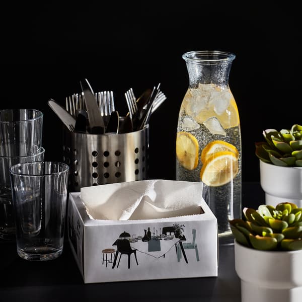 Display of glasses, cutlery, a carafe with water and slices of lemon, white paper napkins and two small plants.
