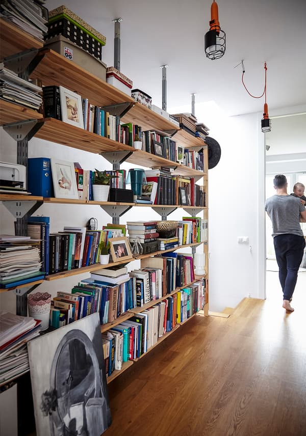 Display shelves in a hallway, loaded with books and boxes, with an adult holding a child walking down the corridor.