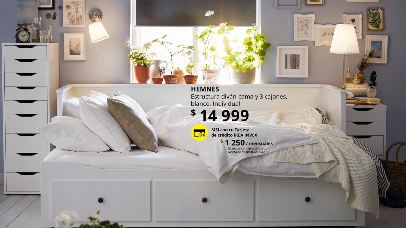 Diván cama HEMNES blanco con tres cajones en un dormitorio, vestido con ropa de cama blanca y rodeado de cómodas blancas.