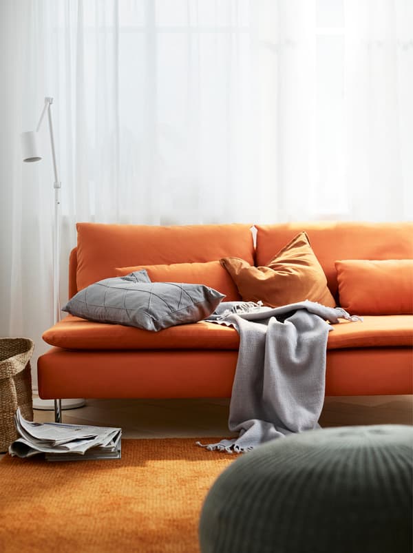 Divano a tre posti SÖDERHAMN arancione con cuscini e una coperta, in un soggiorno con un grande tappeto arancione.