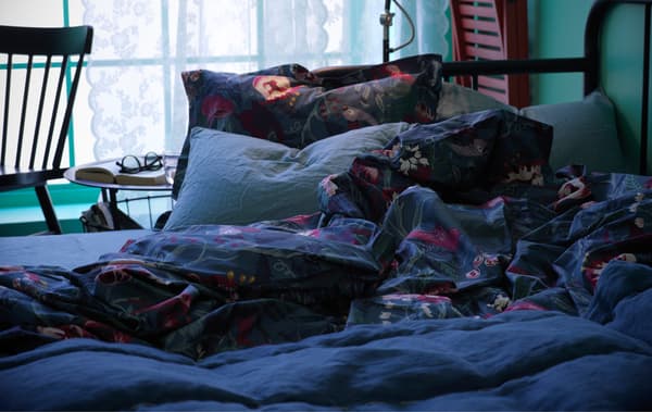 Divano letto FYRESDAL con biancheri a fiori e cuscini. Accanto, un tavolino e una sedia. Alla parete è appesa una sedia pieghevole rossa FRÖSVI.