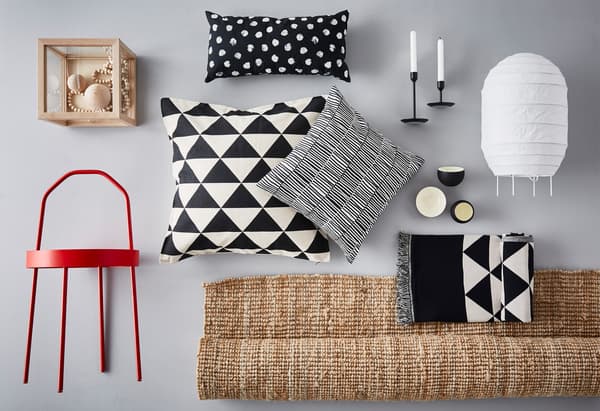 Diversi oggetti messi vicini per creare una moodboard: un tappeto LOHALS, cuscini bianchi e neri, un tavolino rosso BURVIK e candelieri FULLTALIG neri.