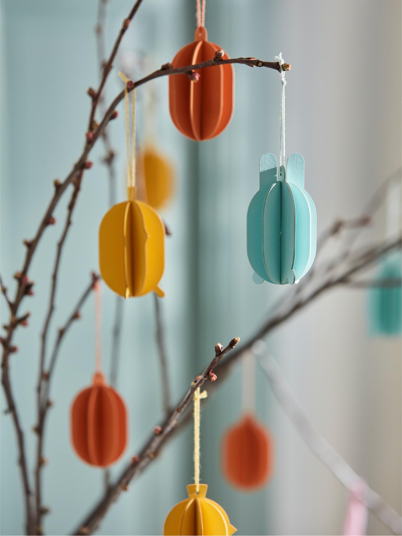 Diversi ramoscelli decorati con delle decorazioni da appendere TJÄRLEK in rosso, giallo e turchese.