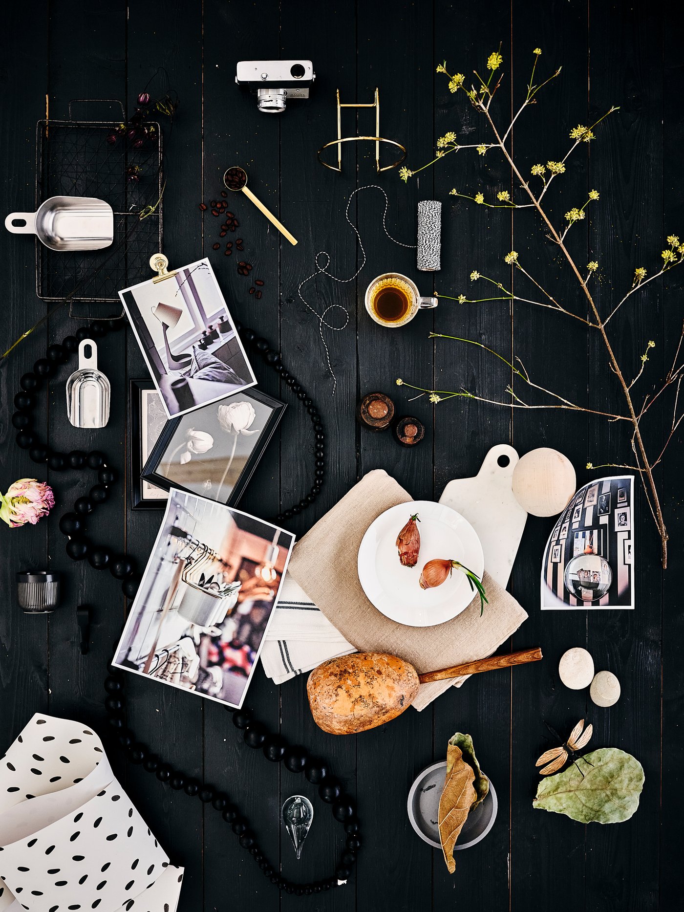 Diversos articles decoratius: un plat blanc OFTAST, mesuradors metàl·lics i un branquilló florit tots dispersos sobre un terra de fusta fosca.