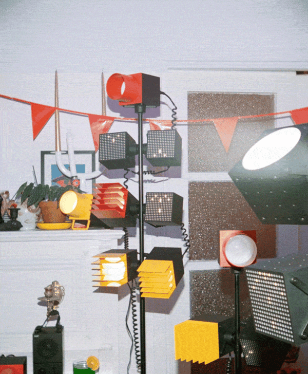Diversos llums de disseny industrial en colors vius (vermell, groc i negre) il·luminen una sala decorada amb banderoles, plantes i objectes decoratius.