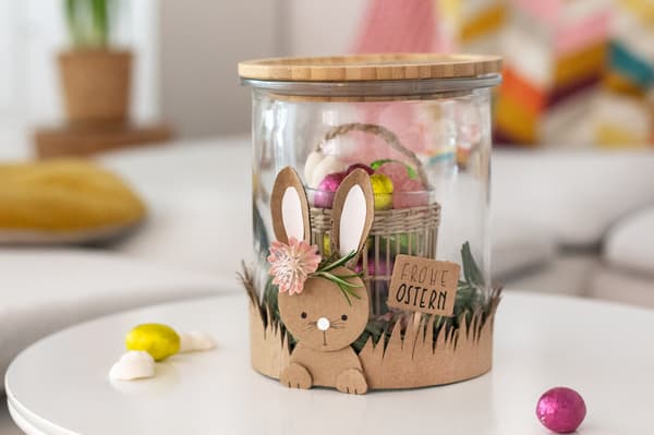 DIY Osterglas als Geschenk für das Osterfest. DAs Glas ist beklebt mit einem aus Pappe ausgeschnittenem Osterhasen. Im Glas befindet sich ein Kleines Teelicht, das aussieht wie ein Körbchen und Süßigkeiten hält. 
