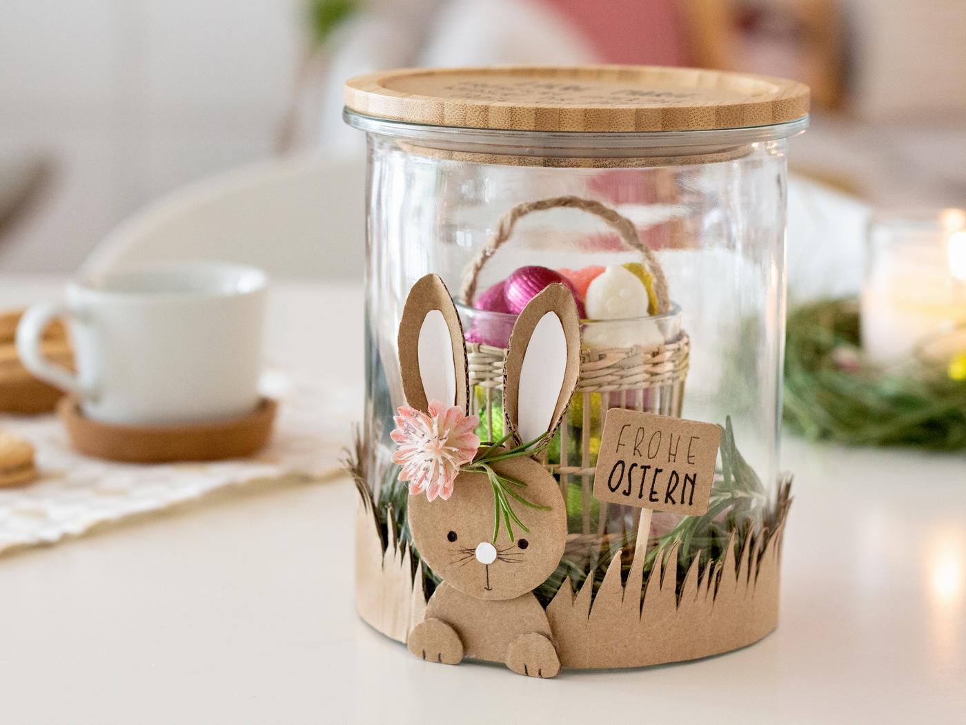 DIY Osterglas als Geschenk für das Osterfest. DAs Glas ist beklebt mit einem aus Pappe ausgeschnittenem Osterhasen. Im Glas befindet sich ein Kleines Teelicht, das aussieht wie ein Körbchen und Süßigkeiten hält. 