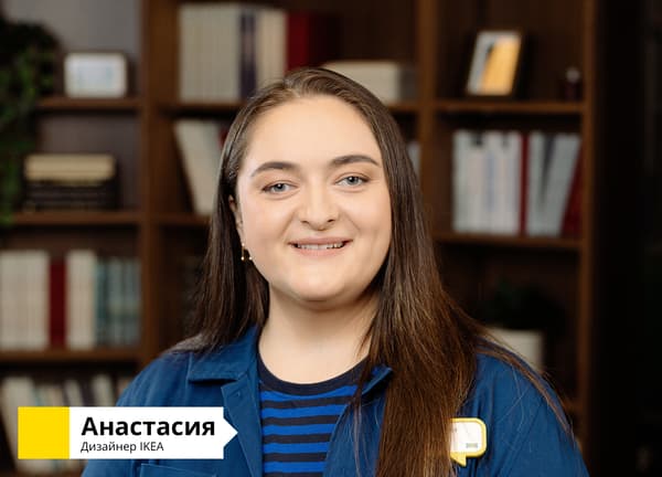 Дизайнер IKEA в синей форме стоит перед тёмным деревянным книжным шкафом. В левом нижнем углу надпись: «Анастасия, дизайнер IKEA».						
