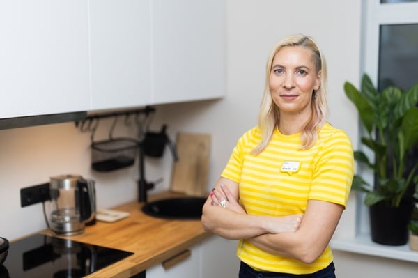 Дизайнер IKEA в жёлтой форме стоит на кухне с белыми фасадами и деревянной столешницей.